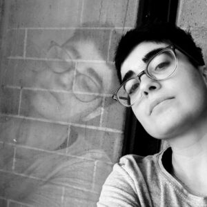Black and white headshot of Amanda Schubert looking into the camera while leaning hear head against a window, which reflects her face