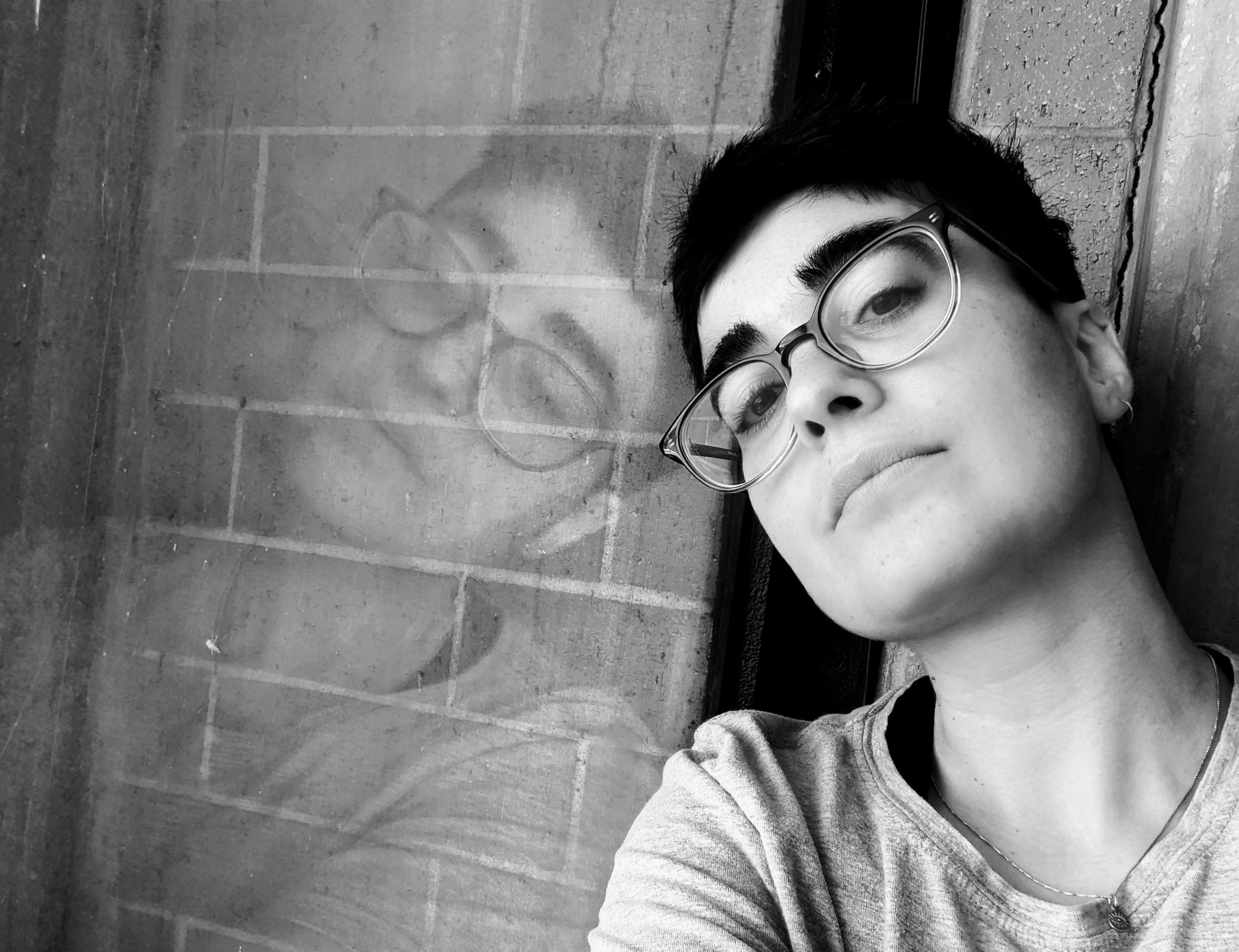 Black and white headshot of Amanda Schubert looking into the camera while leaning hear head against a window, which reflects her face