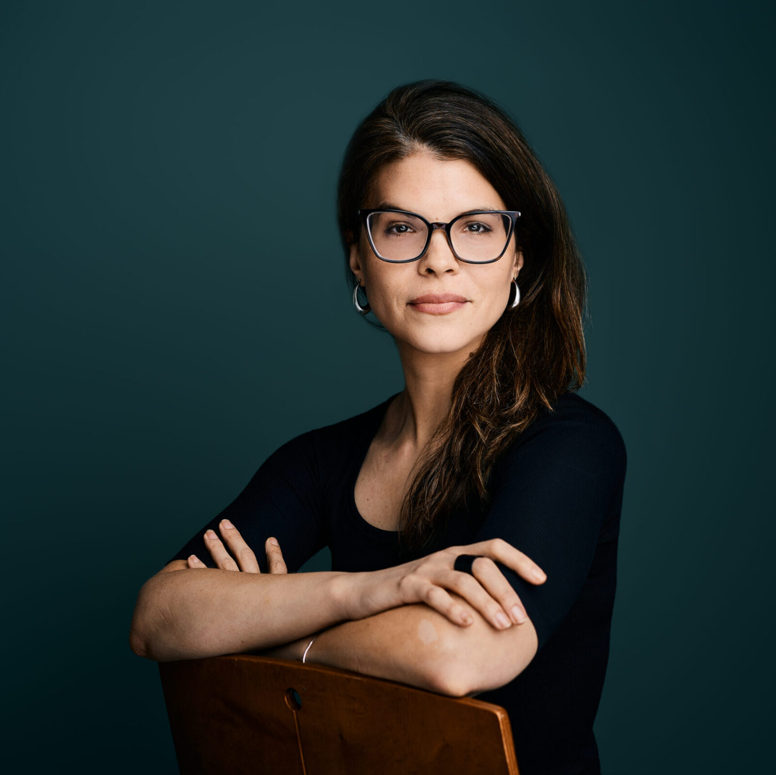 Headshot of Sarah Ann Wells. A studio portrait in front of a dark blue-green backdrop