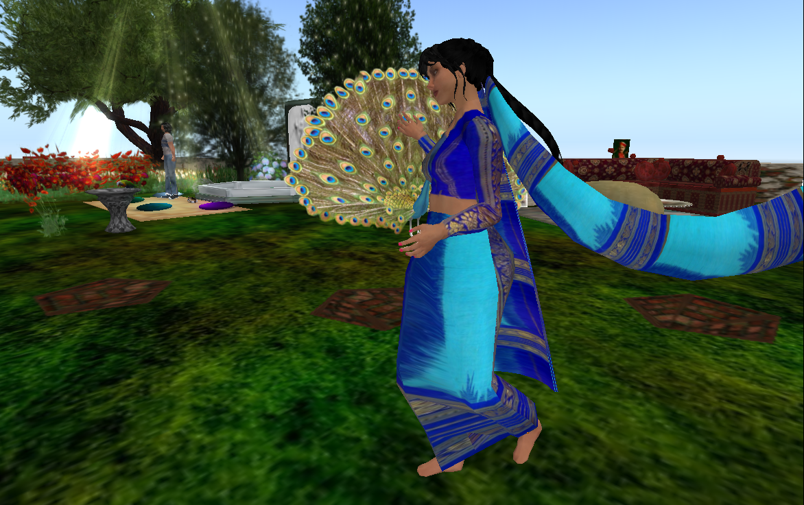 A digitally created image of a person wearing a sari that is alternating klein blue and cyan. The person has red painted nails and long dark hair. A peacock fans his tail behind the person, and they both stand on a pixelated grassy plane. In the background is another person, trees, and red shrubs.